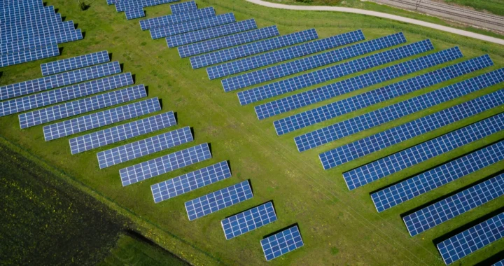 View of a large solar farm with rows of solar panels on green fields, representing the shift toward renewable energy.