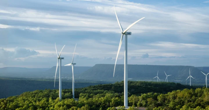 a group of wind turbines on top of a green hillside with a clear sky
