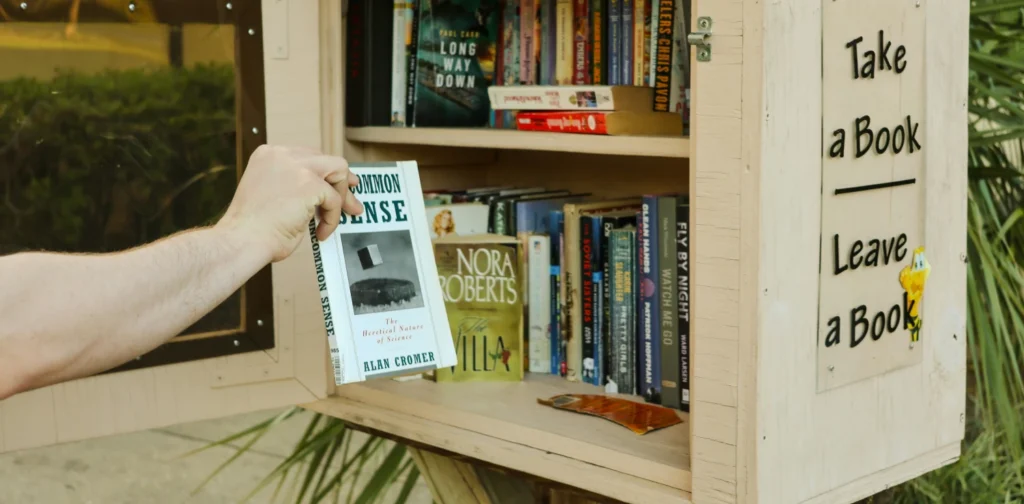 Someone is reaching for a book from a little free library stand
