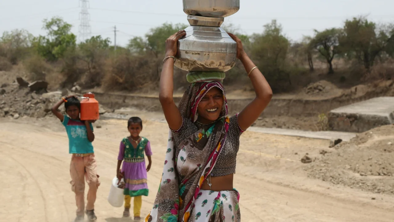 a woman and two children each carrying a bucket of water