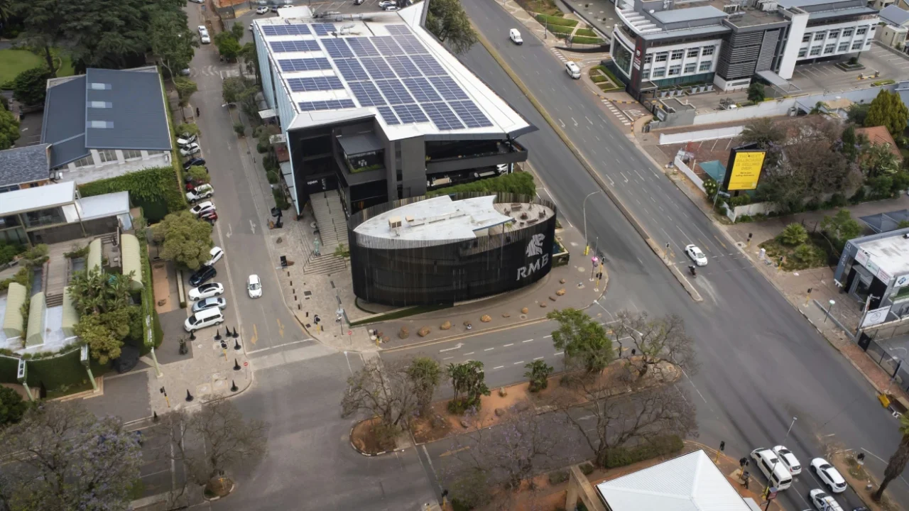 Aerial view of an urban intersection in south africa with modern buildings, one with rooftop solar panels, and light traffic on surrounding streets.