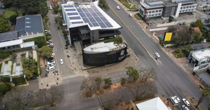 Aerial view of an urban intersection in south africa with modern buildings, one with rooftop solar panels, and light traffic on surrounding streets.