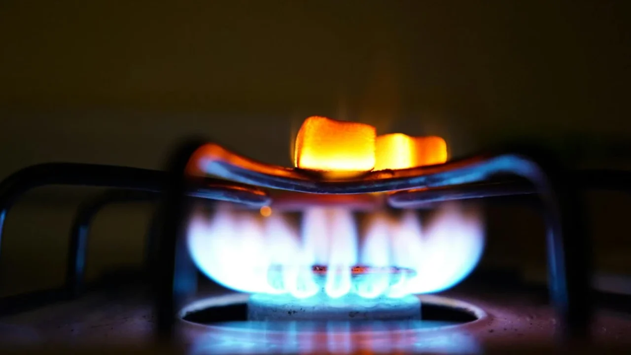 Blue and orange gas flame on a circular kitchen stove burner against a dark background.