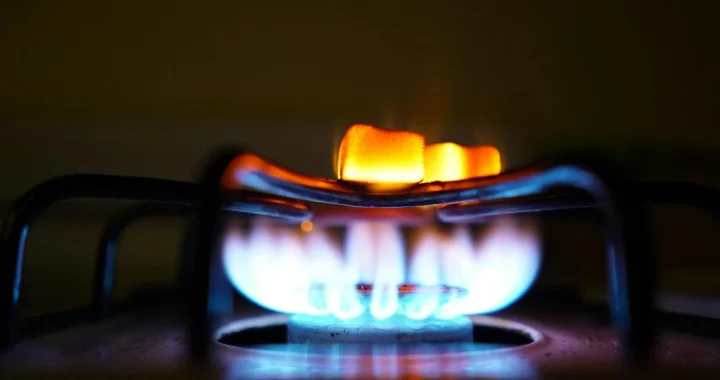 Blue and orange gas flame on a circular kitchen stove burner against a dark background.