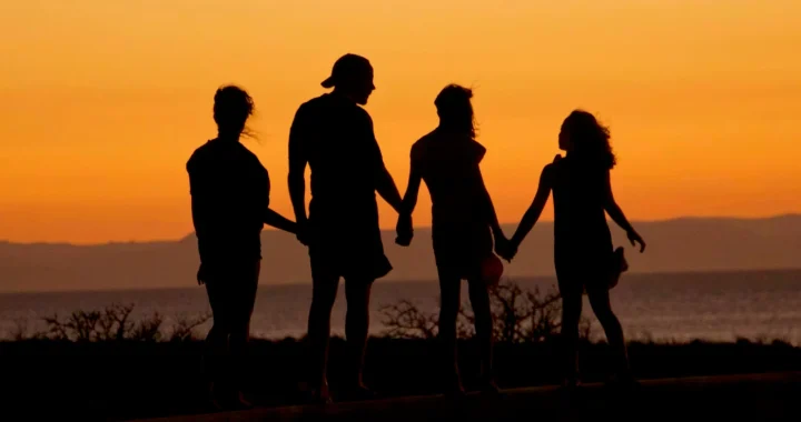a silhouette of a family of four against a sunset sky