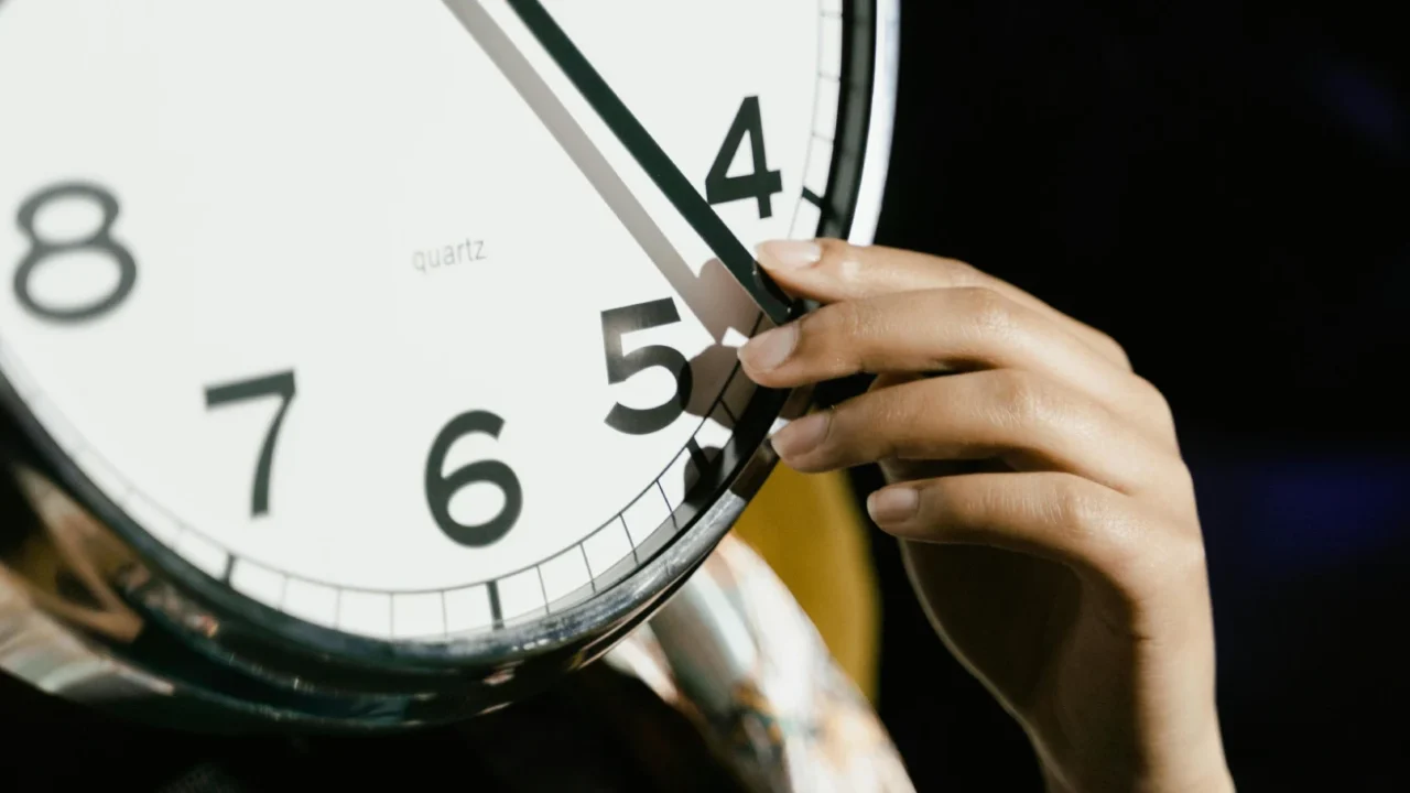 a close up of a clock face with a human hand holding one of the clock hands