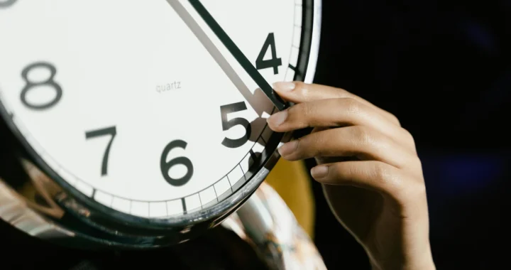a close up of a clock face with a human hand holding one of the clock hands