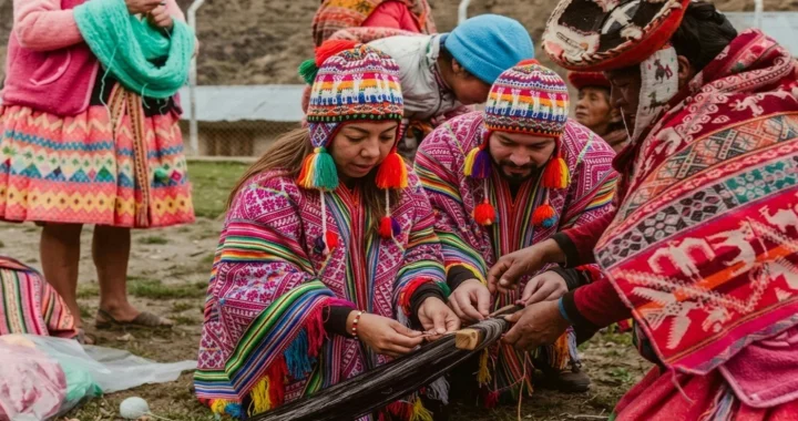 Several individuals in traditional clothing working together on a weaving loom outdoors, while others stand nearby observing.