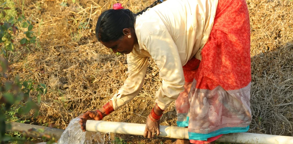 a woman bending over to collect water from a pipe