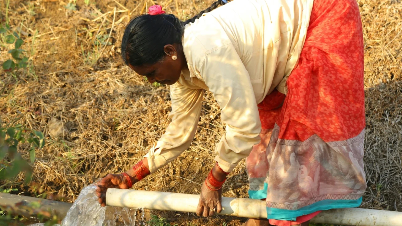 a woman bending over to collect water from a pipe