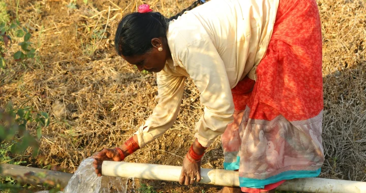 a woman bending over to collect water from a pipe