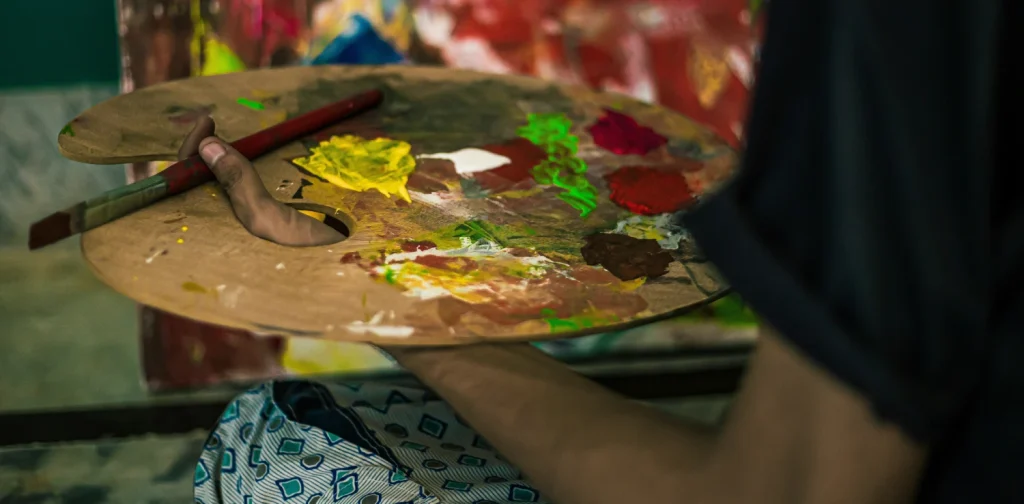 A hand holding a palette with various colors of paint