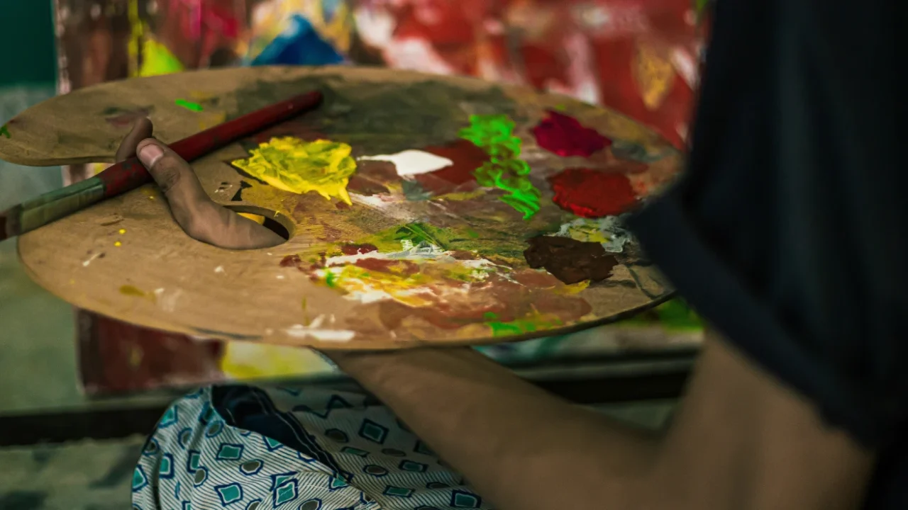 A hand holding a palette with various colors of paint