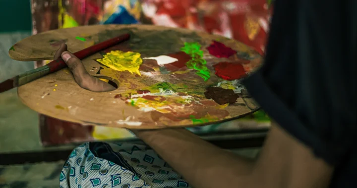A hand holding a palette with various colors of paint
