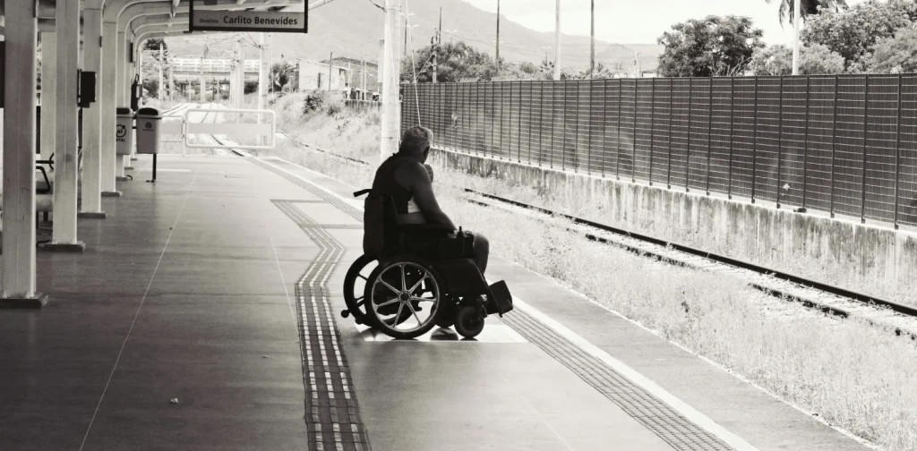 a grayscale photo of a person sitting on a wheelchair on a train platform