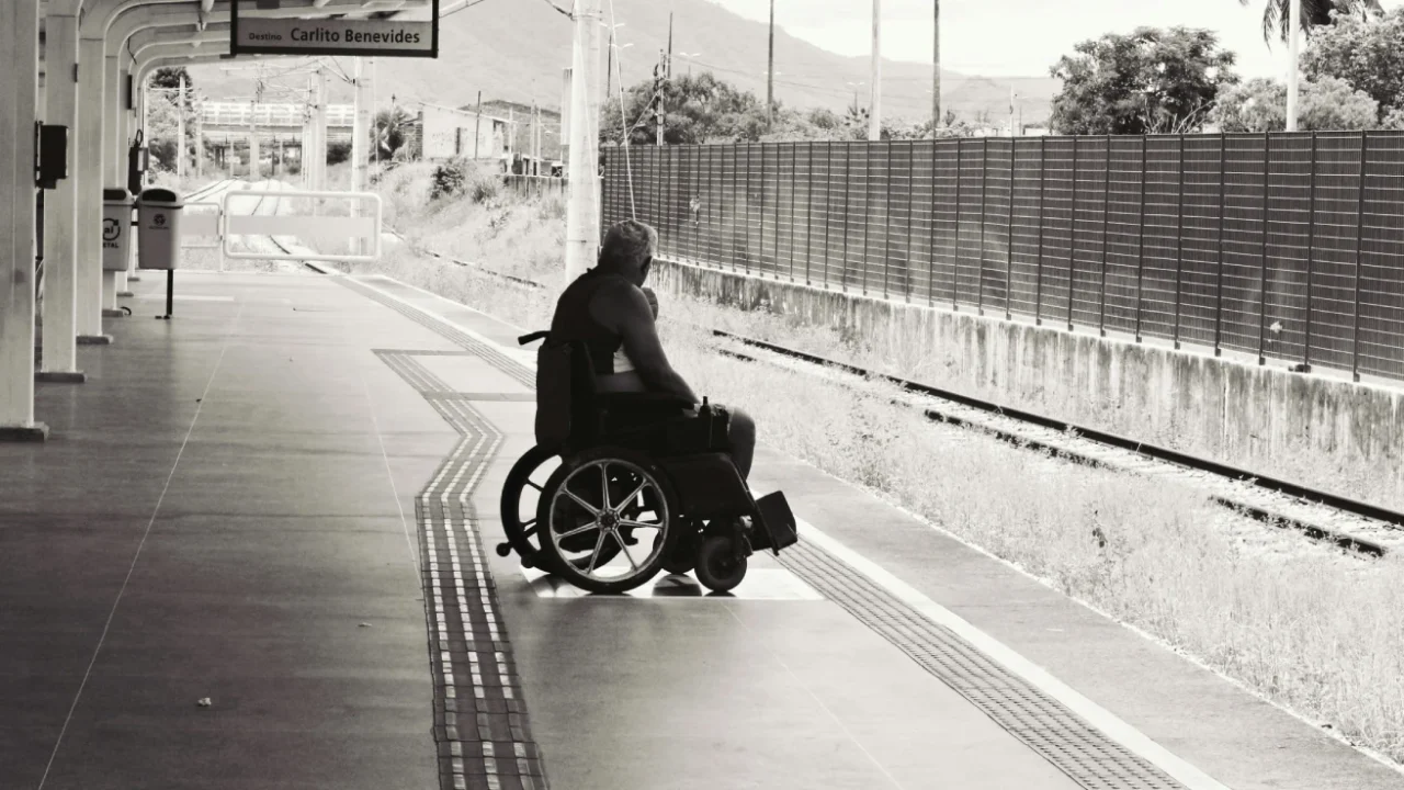 a grayscale photo of a person sitting on a wheelchair on a train platform