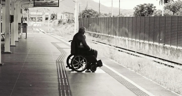 a grayscale photo of a person sitting on a wheelchair on a train platform