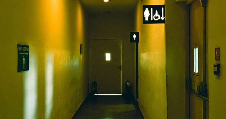 a hallway with yellow lighting with signs for a male restroom further back and female restroom and disability signs side by side