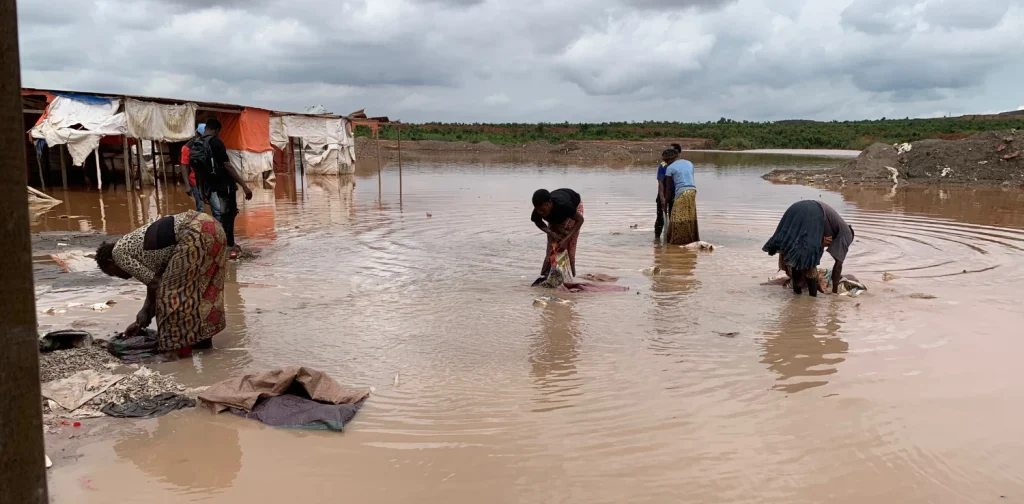 Four African women washing cobalt in a muddy body of water.