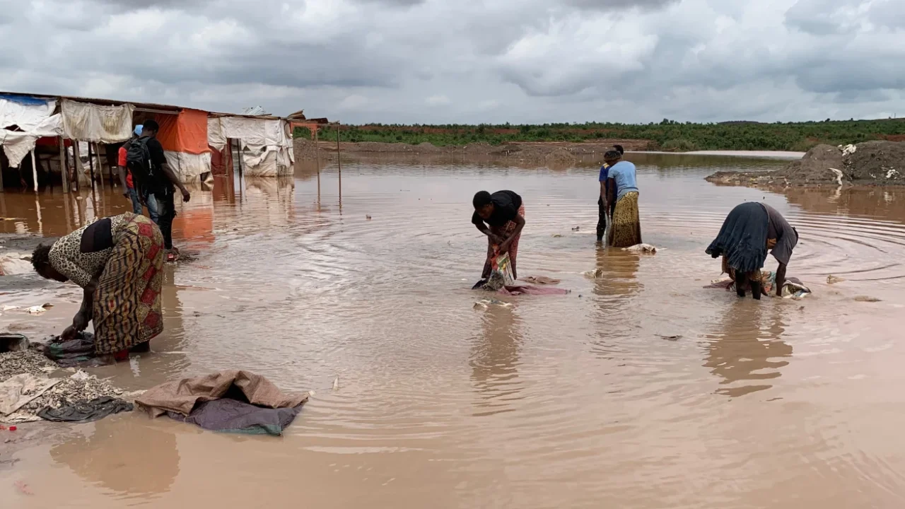 Four African women washing cobalt in a muddy body of water.