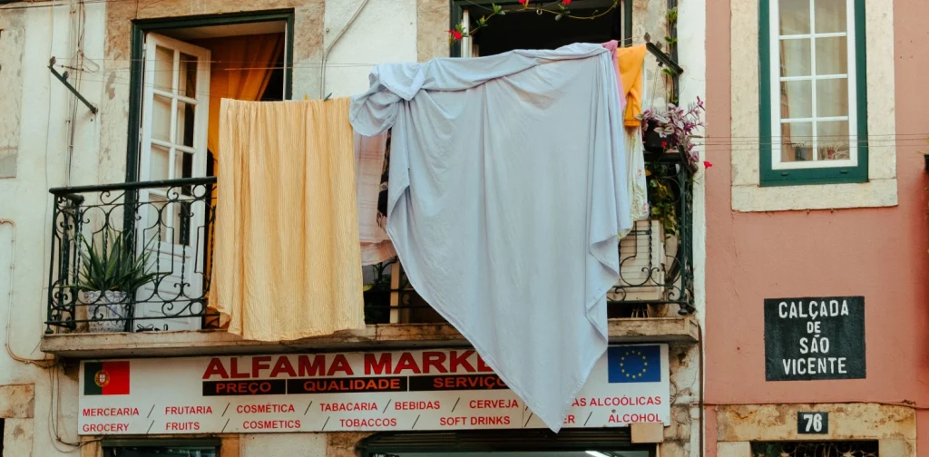 laundered sheets hanging from the window on the second floor of a local market store in alfama, lisbon