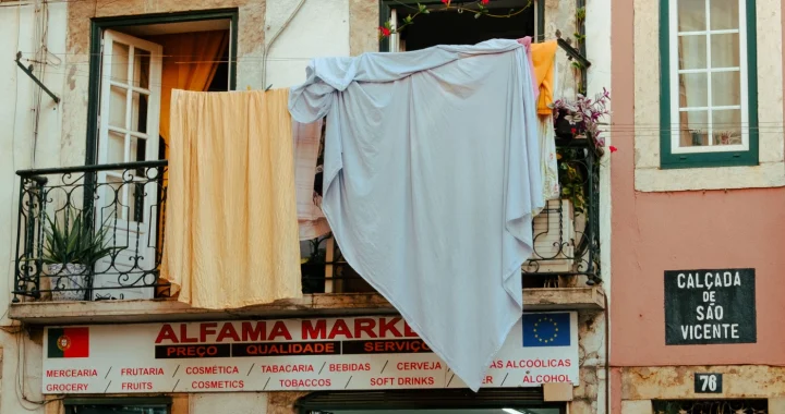 laundered sheets hanging from the window on the second floor of a local market store in alfama, lisbon