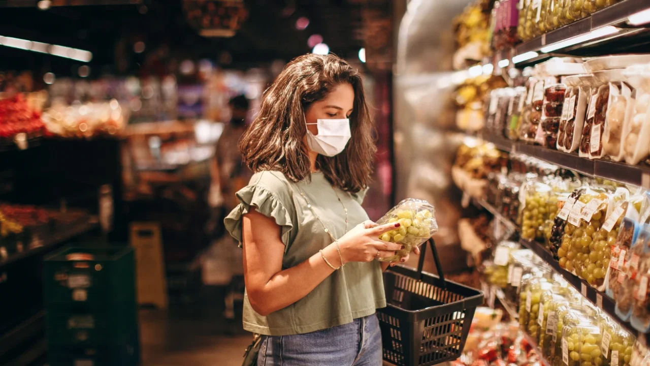 Young woman in a mask selecting fresh fruits in a supermarket produce aisle.