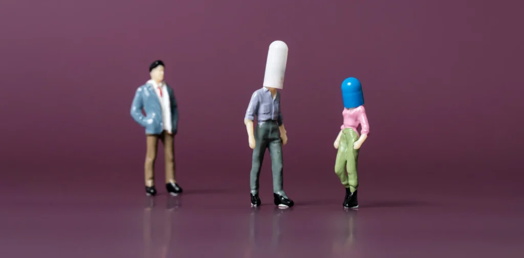 three figurines of people, two with their heads covered in a pill each and one without.