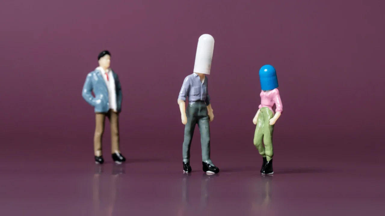 three figurines of people, two with their heads covered in a pill each and one without.