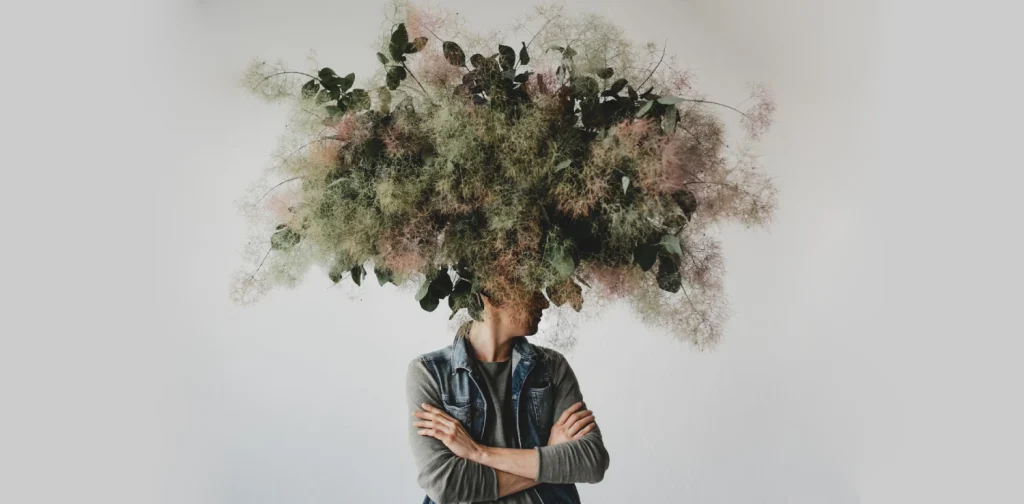 Large decorative bouquet made of green leaves and moss hangs over man's head