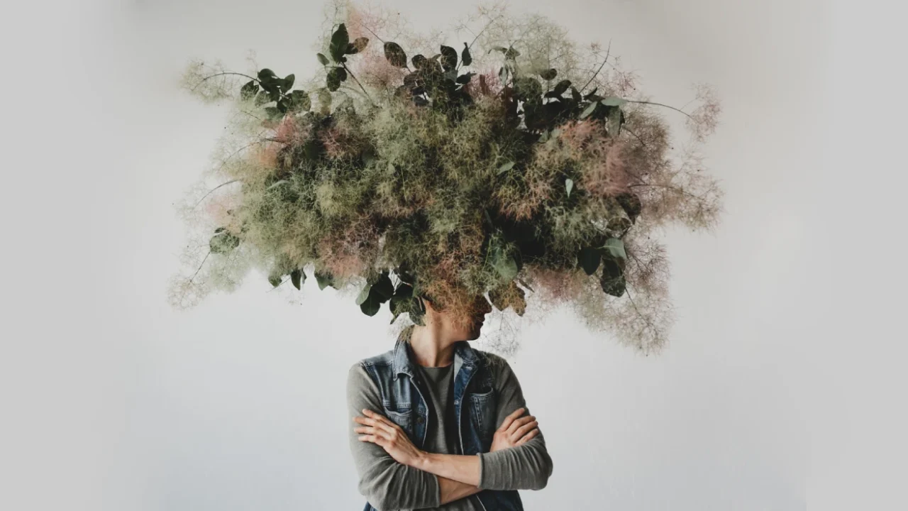 Large decorative bouquet made of green leaves and moss hangs over man's head