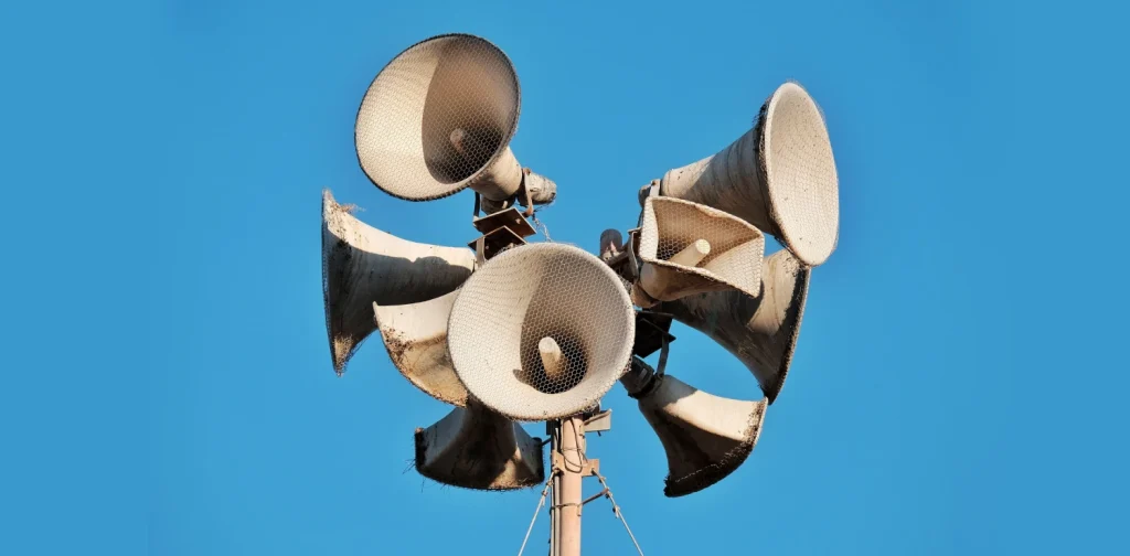 Close-up of multiple aged megaphones on a pole against a clear blue sky.