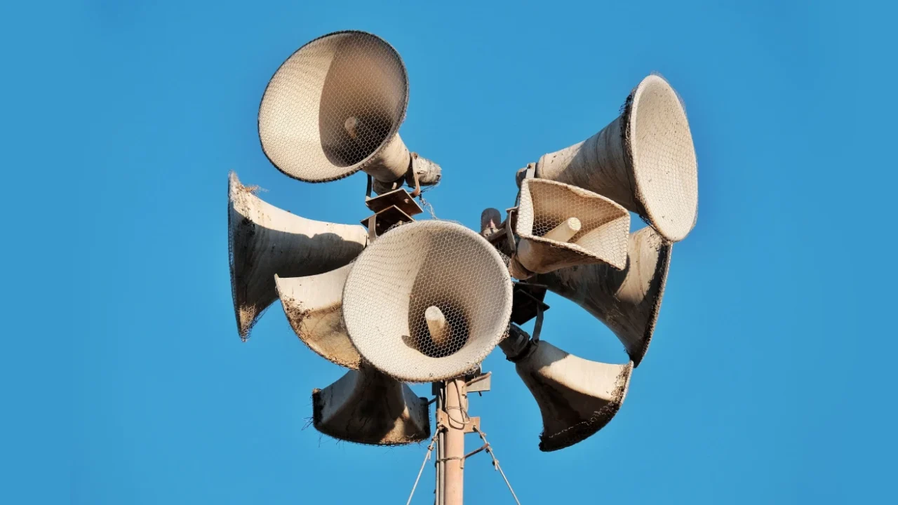 Close-up of multiple aged megaphones on a pole against a clear blue sky.