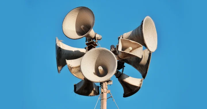 Close-up of multiple aged megaphones on a pole against a clear blue sky.
