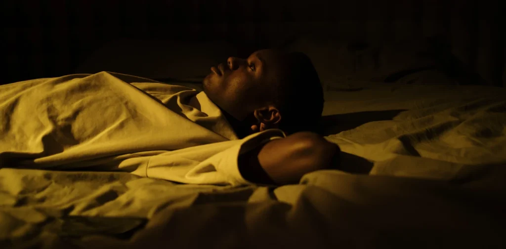 a man lying wide awake on a bed in the dark in a quiet bedroom