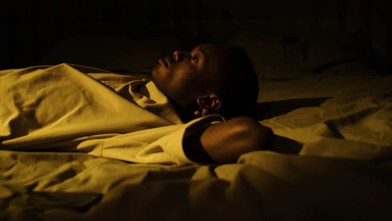 a man lying wide awake on a bed in the dark in a quiet bedroom