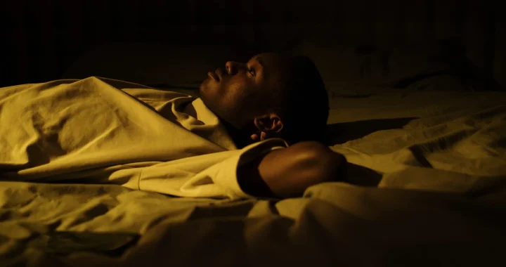 a man lying wide awake on a bed in the dark in a quiet bedroom