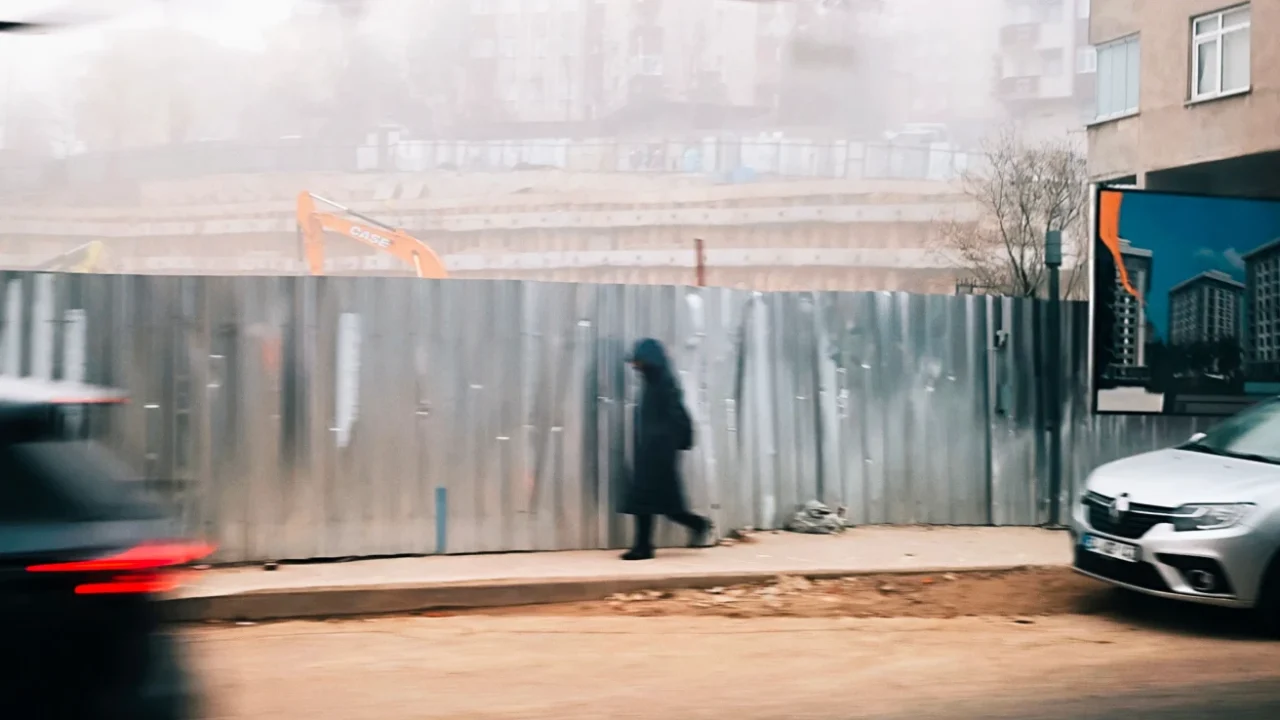 a pedestrian walking at the sidewalk with construction by the side of the road and car traffic on the street