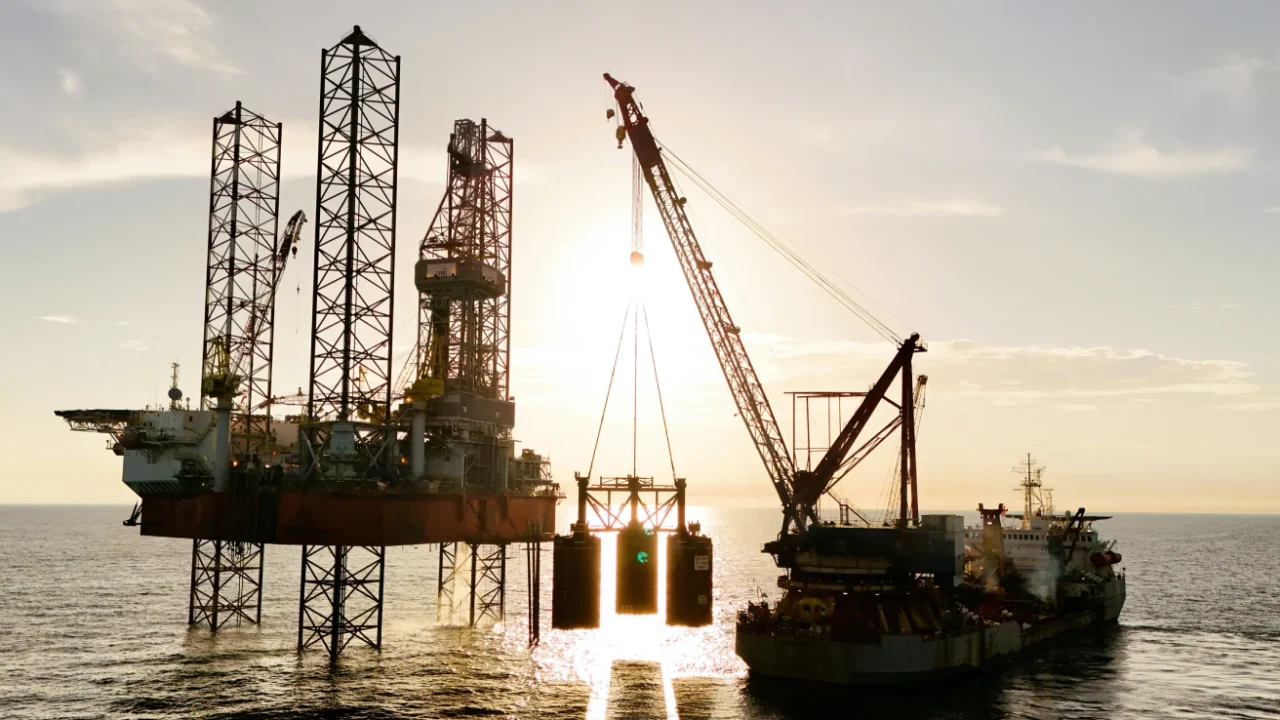 Offshore oil drilling platform and construction vessel operating at sea during sunset with a large care lifting equipment.