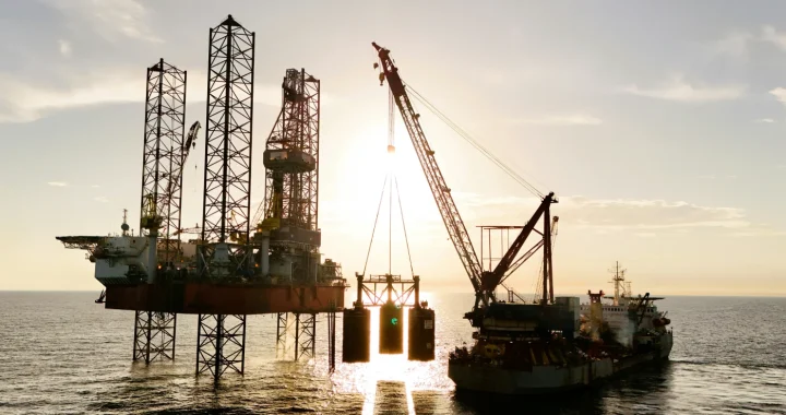 Offshore oil drilling platform and construction vessel operating at sea during sunset with a large care lifting equipment.