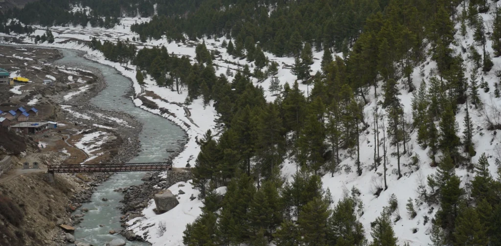 snow covered alley in the himalaya, a river stream, and a bridge going across the river