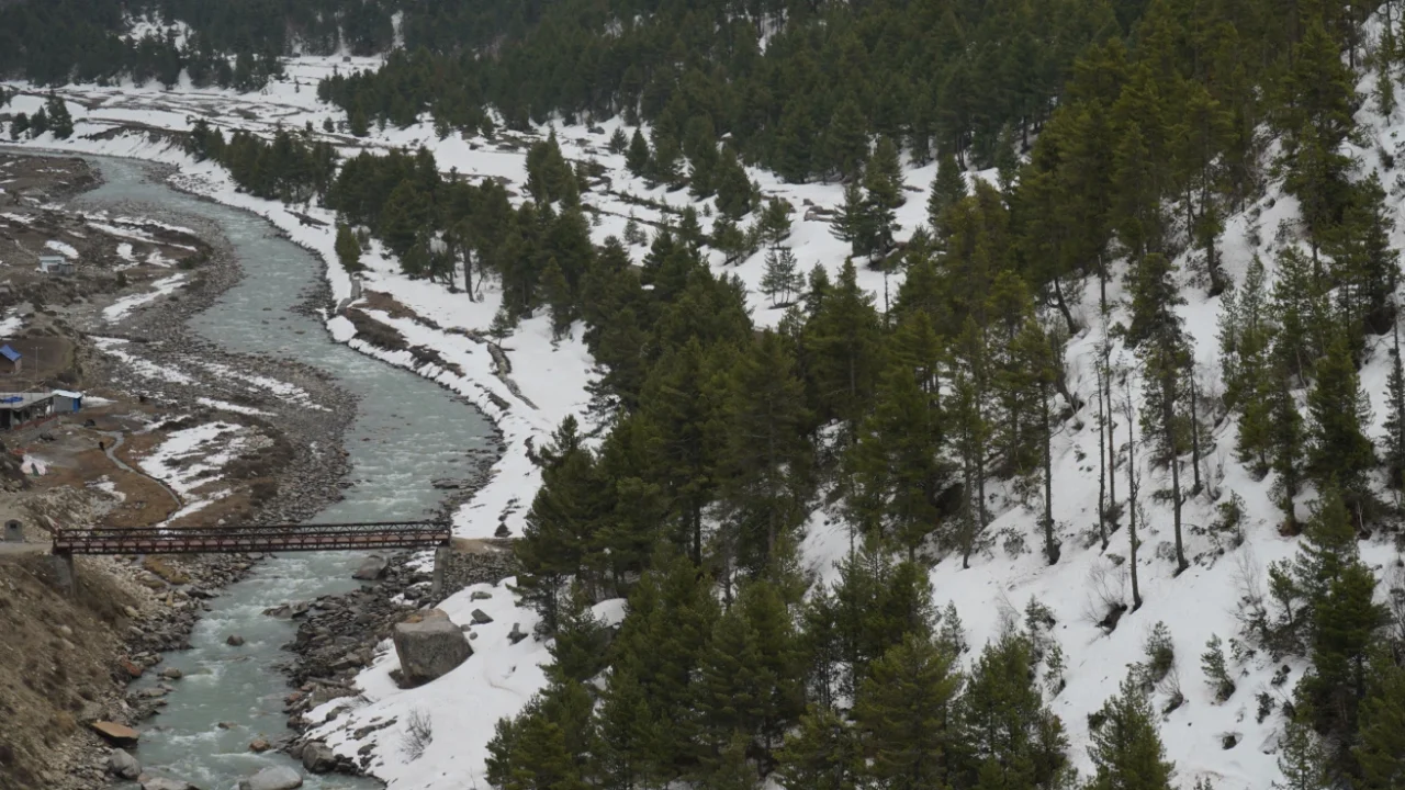 snow covered alley in the himalaya, a river stream, and a bridge going across the river