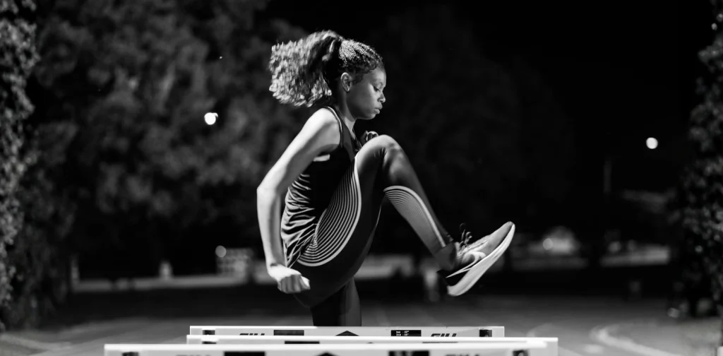 a side portrait of a black female athlete practicing on a hurdle