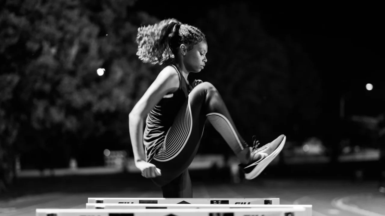 a side portrait of a black female athlete practicing on a hurdle