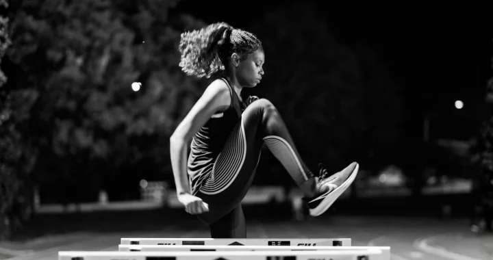 a side portrait of a black female athlete practicing on a hurdle