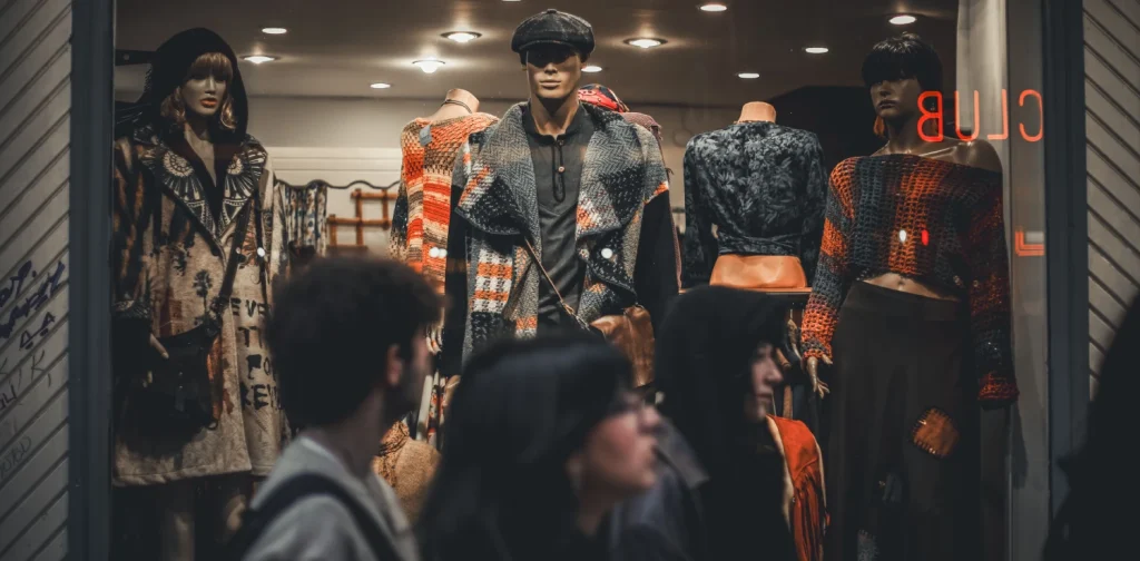 A clothing store displays trendy outfits on mannequins with people passing by the store.