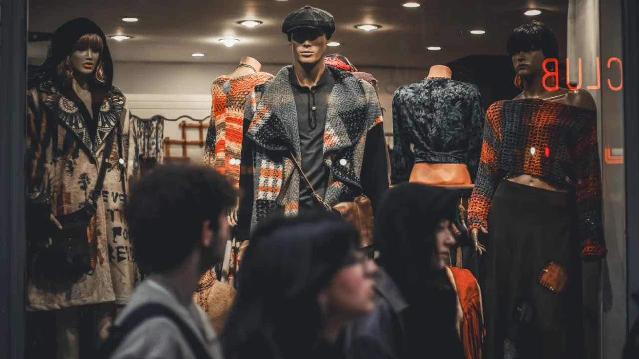 A clothing store displays trendy outfits on mannequins with people passing by the store.
